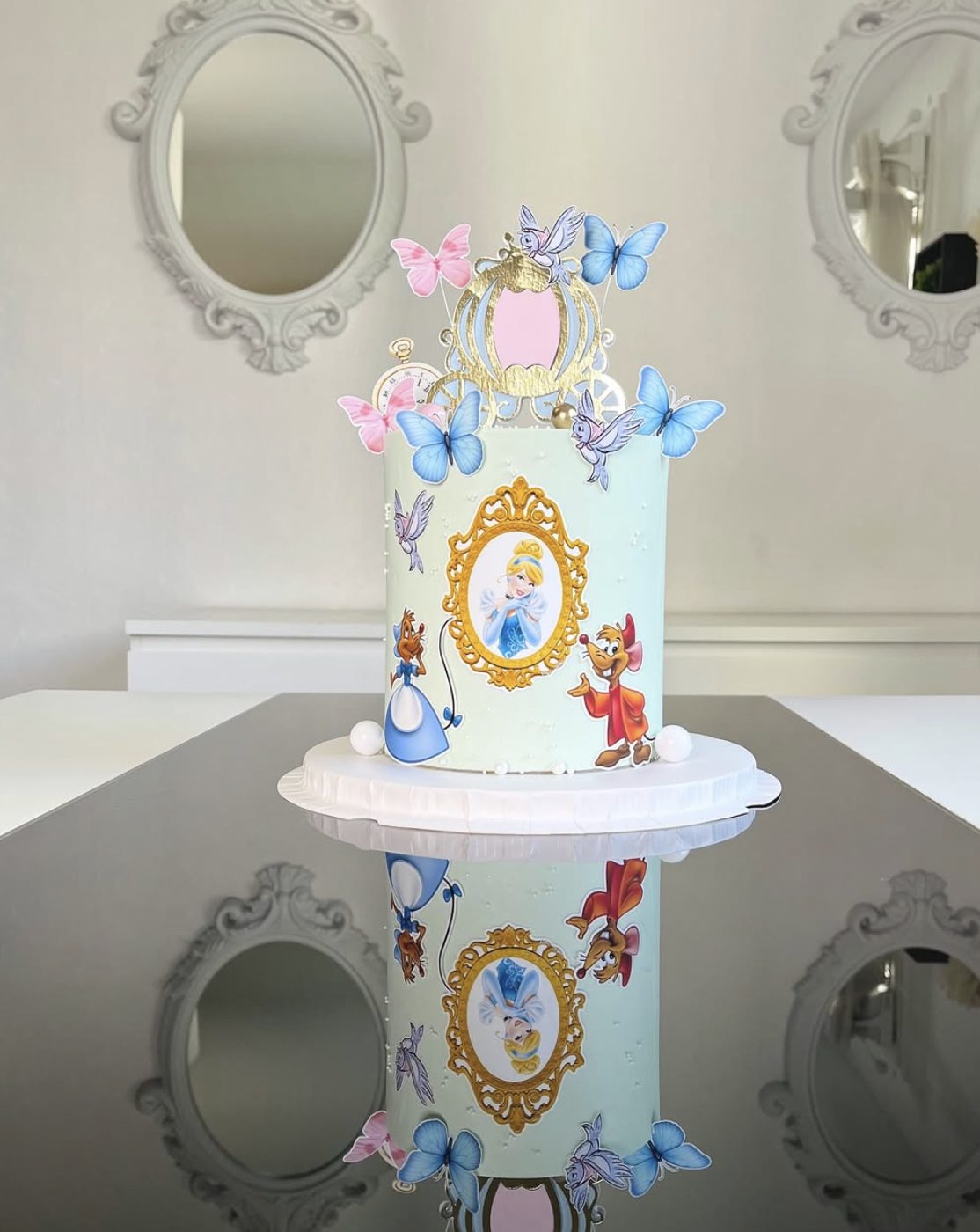 This Cinderella birthday cake is simple, pretty, and full of sweet fairytale details. The pale blue cake, gold carriage topper, clock accent, butterflies, birds, Cinderella portrait, and Jaq and Gus details make it feel magical without needing a large tiered design.