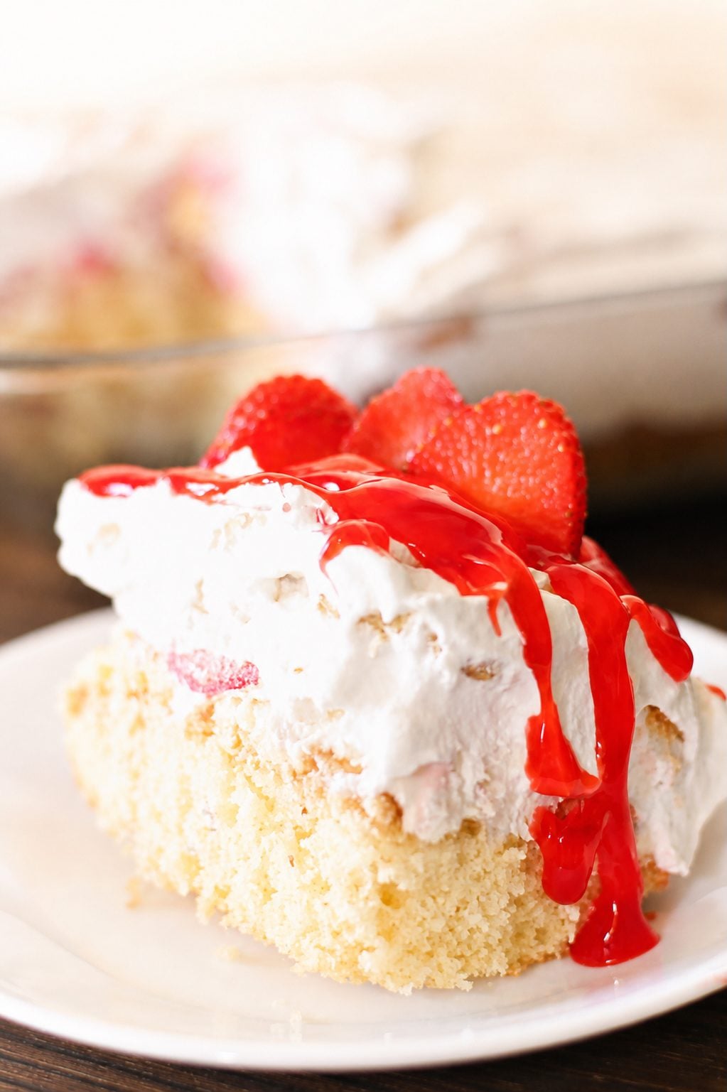 Easy strawberry shortcake lasagna slice with whipped cream, fresh strawberries, and strawberry glaze on a white plate.
