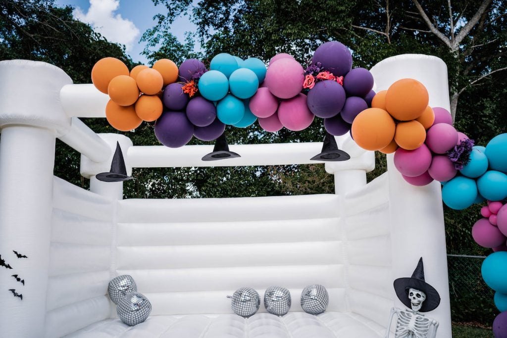 Colorful balloon garland with hanging witch hats adorn the white bounce house
