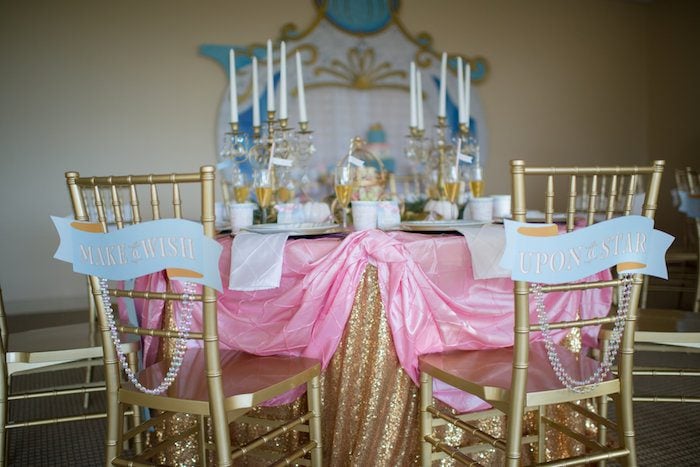 Cinderella party table with gold sequin tablecovers, gold chairs with signs, and candelabras